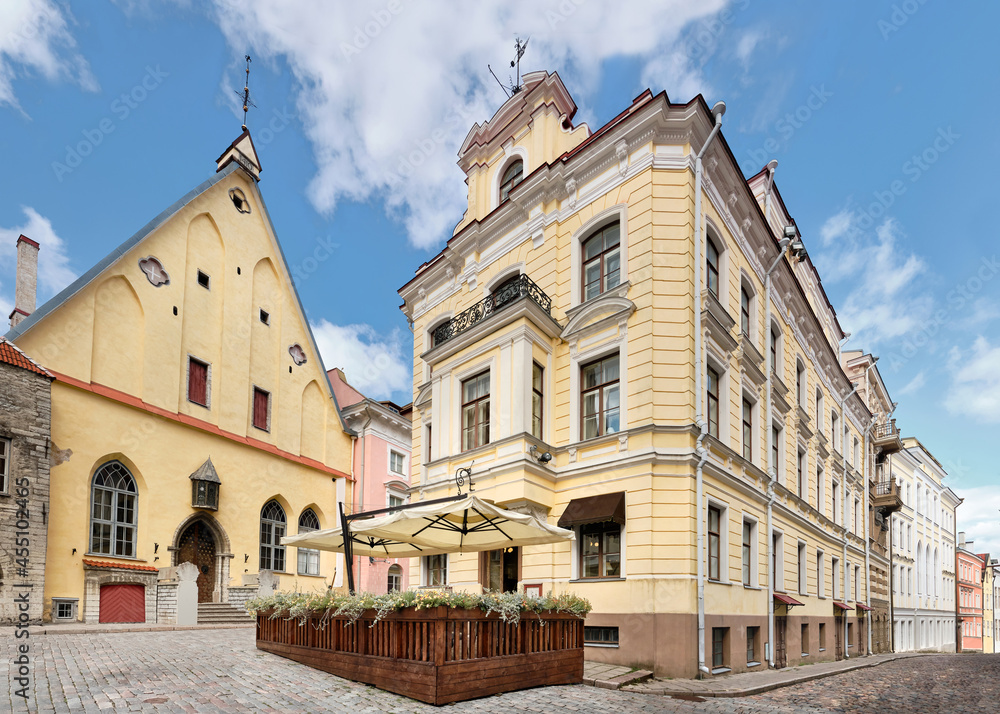 Medieval Tallinn, panoramic image of old town. Ancient houses on cobbled street in medieval center. Wooden terrasse of outdoor cafe or restaurant. Daylight, blue sky with cumulous clouds.