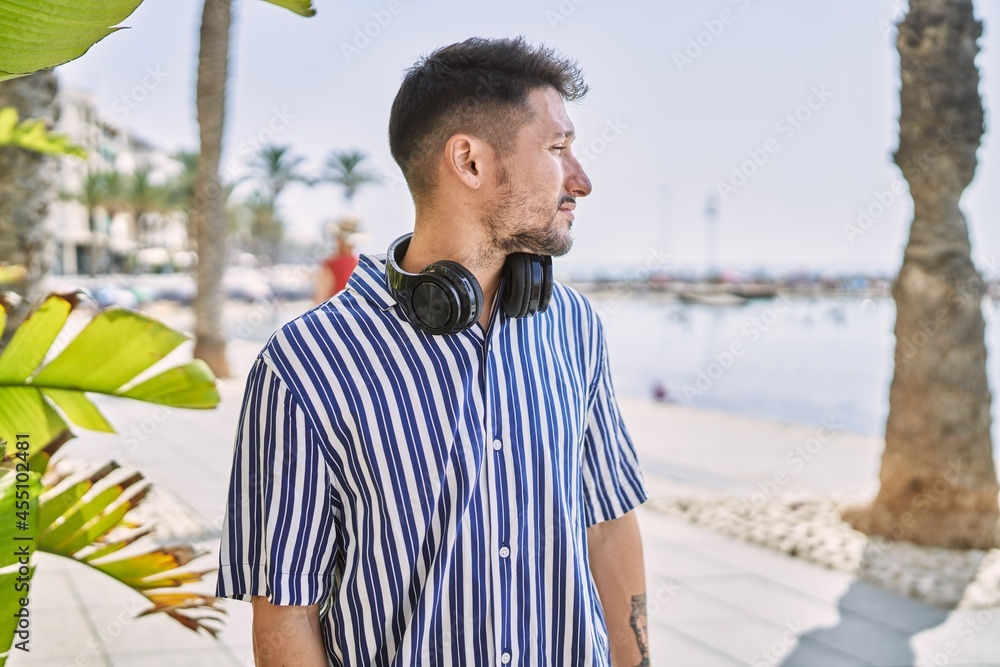 Young handsome man listening to music using headphones outdoors looking to side, relax profile pose with natural face with confident smile.