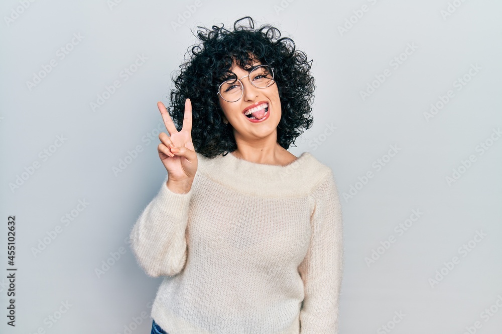 Young middle east woman wearing casual white tshirt smiling with happy face winking at the camera doing victory sign. number two. Young middle east woman wearing casual white tshirt smiling with happy face winking at the camera doing victory sign. number two.