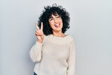 Young middle east woman wearing casual white tshirt smiling with happy face winking at the camera doing victory sign. number two.