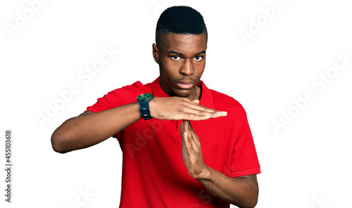 Young african american man wearing casual red t shirt doing time out gesture with hands, frustrated and serious face