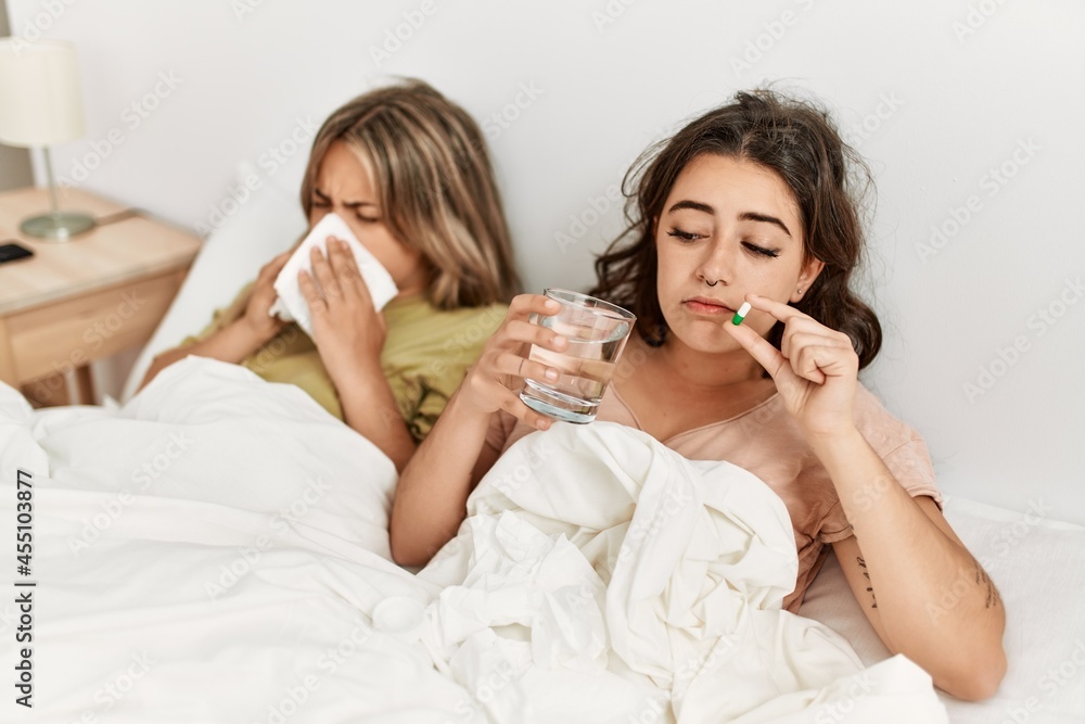 Young ill couple using napkin and eating pills lying on the bed at home. Young ill couple using napkin and eating pills lying on the bed at home.