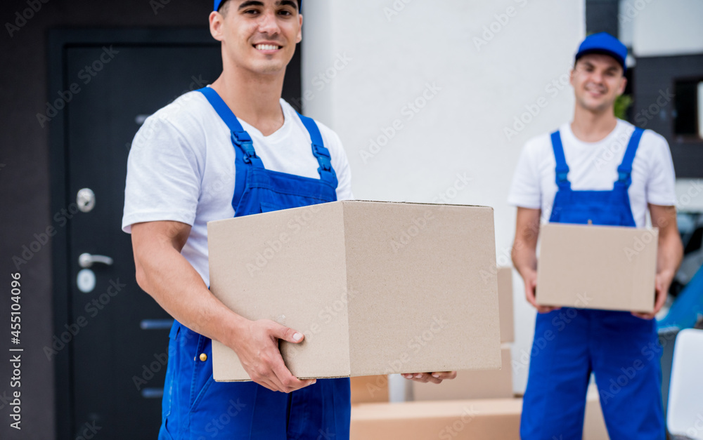 Two removal company workers are loading boxes into a minibus. Two removal company workers are loading boxes into a minibus.