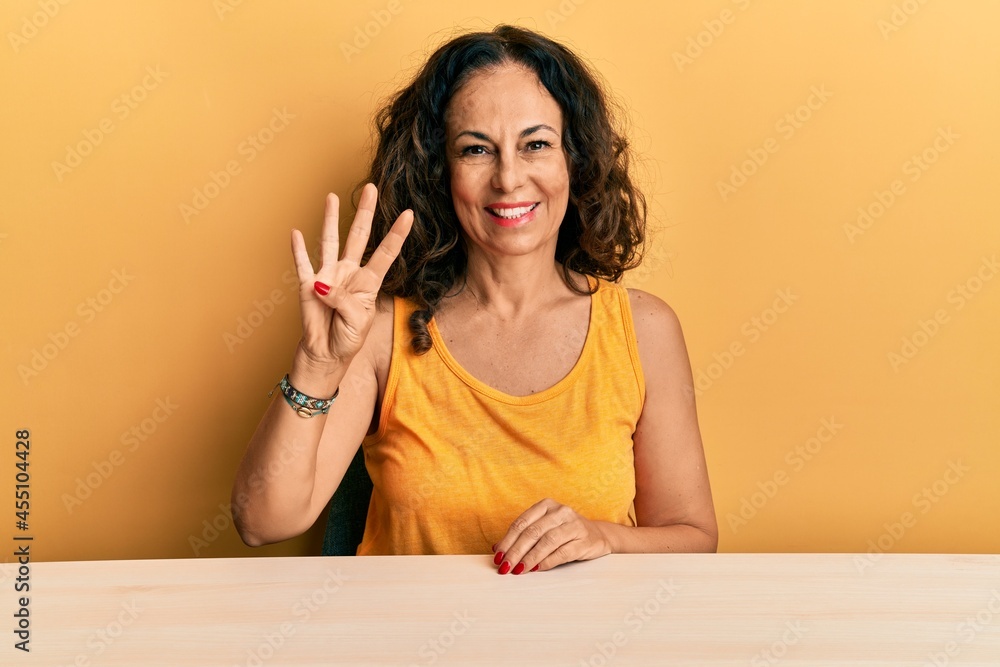 Beautiful middle age woman wearing casual clothes sitting on the table showing and pointing up with fingers number four while smiling confident and happy. Beautiful middle age woman wearing casual clothes sitting on the table showing and pointing up with fingers number four while smiling confident and happy.