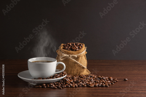 white cup of hot coffee with smoke with coffee beans and sackcloth full of coffee beans with rope