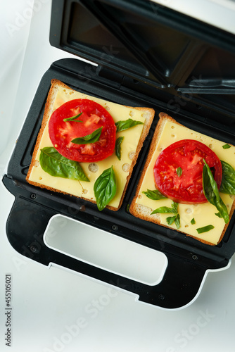 Sandwich in an electric sandwich maker before cooking, bread, cheese and tomatoes with basil photo