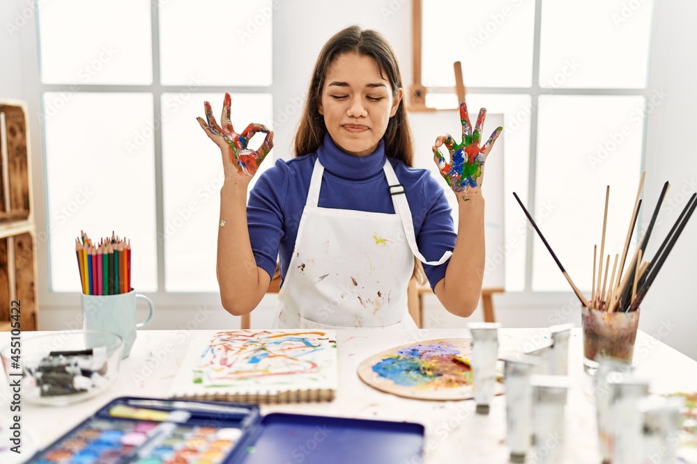 Young brunette woman at art studio with painted hands relax and smiling with eyes closed doing meditation gesture with fingers. yoga concept. Young brunette woman at art studio with painted hands relax and smiling with eyes closed doing meditation gesture with fingers. yoga concept.