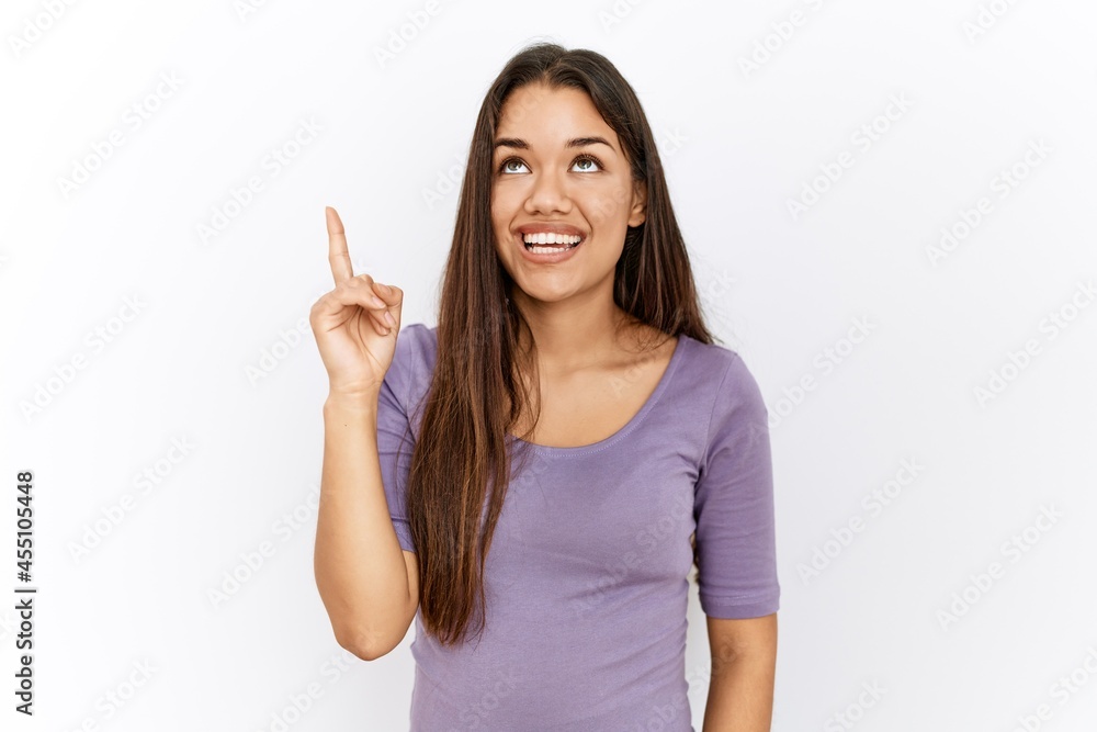 Young brunette woman standing by isolated background pointing finger up with successful idea. exited and happy. number one.