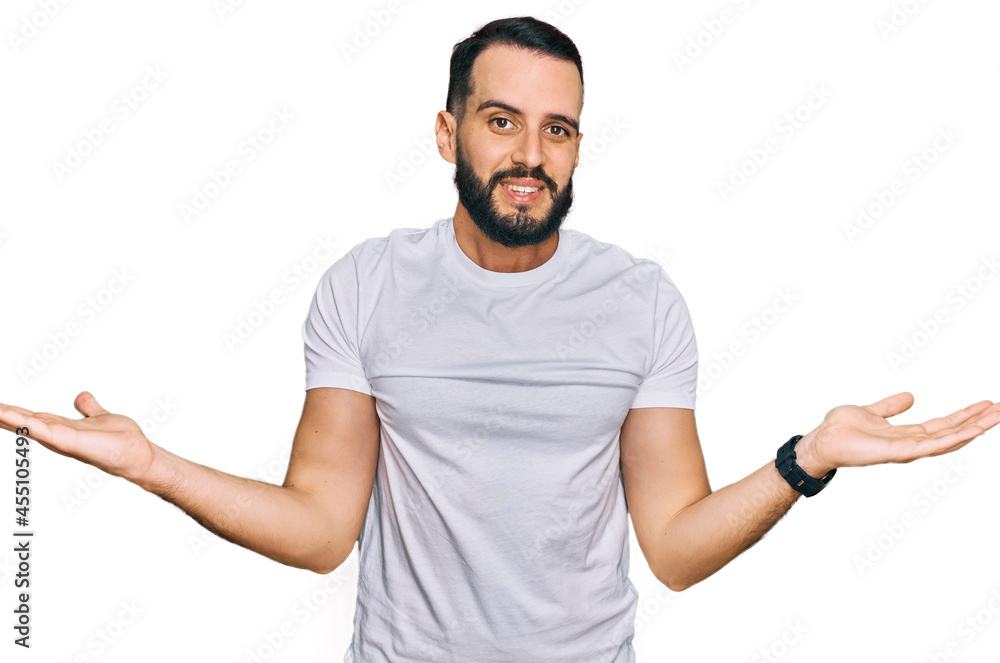 Young man with beard wearing casual white t shirt smiling showing both hands open palms, presenting and advertising comparison and balance Young man with beard wearing casual white t shirt smiling showing both hands open palms, presenting and advertising comparison and balance