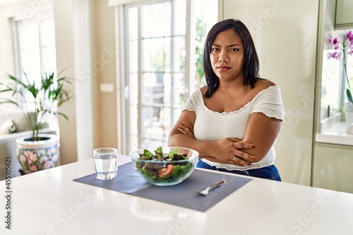 Young hispanic woman eating healthy salad at home skeptic and nervous  disapproving expression on face with crossed arms. negative person.