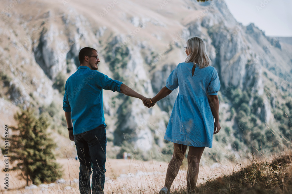 Rear view of couple in love who standing on mountain, watching around beautiful mountain scenery and tenderly embracing each other. Pleasant moment of hugs while walking in the fresh air. Rear view of couple in love who standing on mountain, watching around beautiful mountain scenery and tenderly embracing each other. Pleasant moment of hugs while walking in the fresh air.