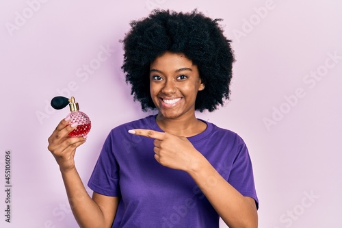 Young african american woman holding perfume smiling happy pointing with hand and finger