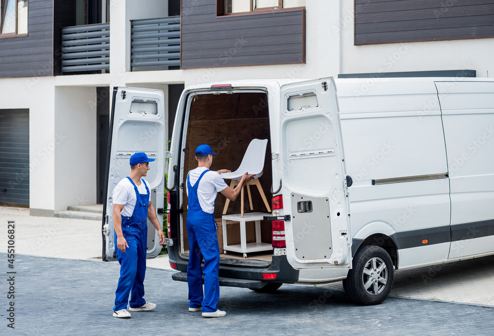Two removal company workers are loading boxes and furniture into a minibus. Two removal company workers are loading boxes and furniture into a minibus.