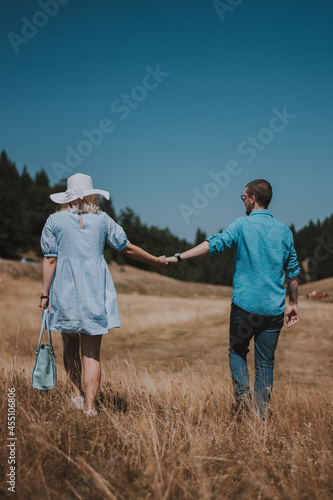 rear view of young couple walking hand in hand walking away. Man and woman walking in the mountain while holding hands. © Dinno