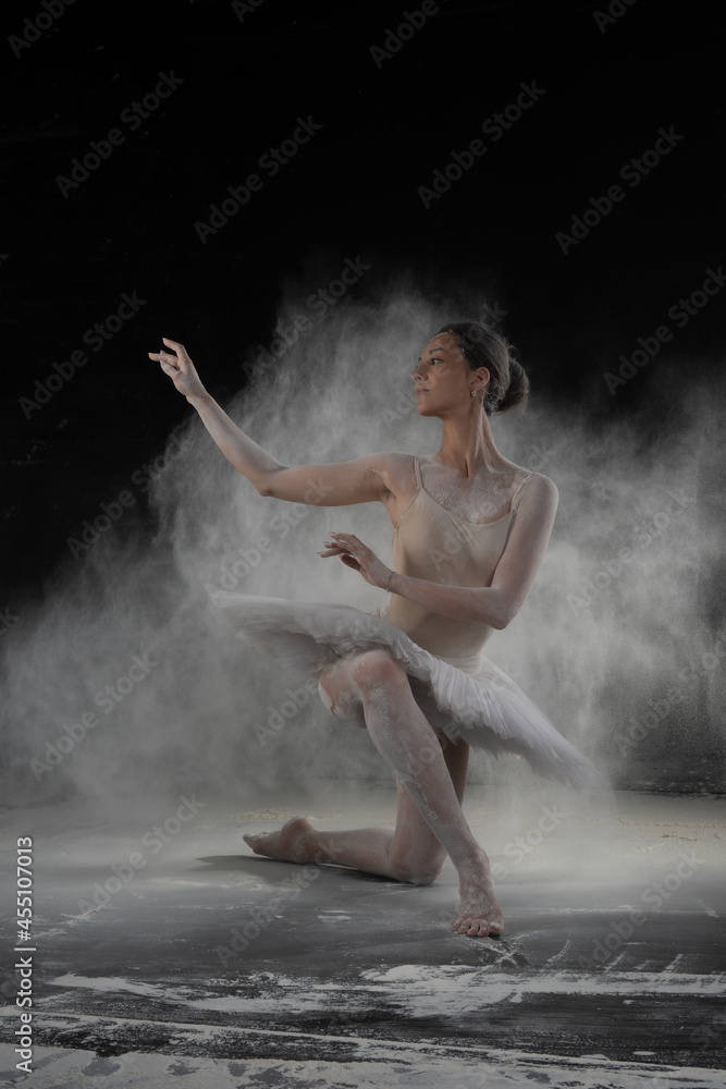 beautiful ballerina dancing in white flour near a black wall
