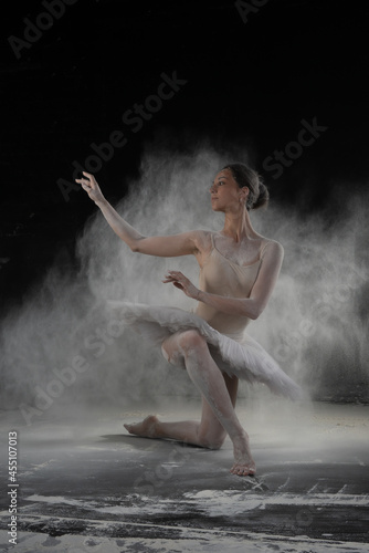 Fototapeta Naklejka Na Ścianę i Meble -  beautiful ballerina dancing in white flour near a black wall