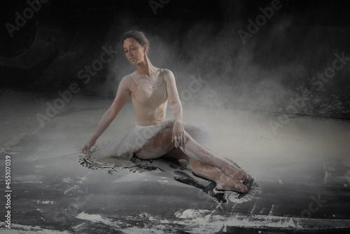 Fototapeta Naklejka Na Ścianę i Meble -  beautiful ballerina dancing in white flour near a black wall
