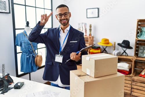 African american man working as manager at retail boutique smiling amazed and surprised and pointing up with fingers and raised arms. © Krakenimages.com