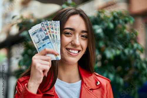 Young hispanic woman smiling happy holding peruvian sol banknotes at the city.