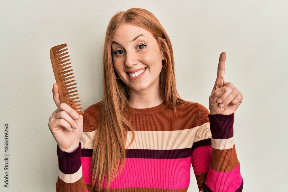 Young irish woman styling hair using comb surprised with an idea or question pointing finger with happy face, number one Young irish woman styling hair using comb surprised with an idea or question pointing finger with happy face, number one