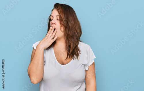 Young plus size woman wearing casual white t shirt bored yawning tired covering mouth with hand. restless and sleepiness.