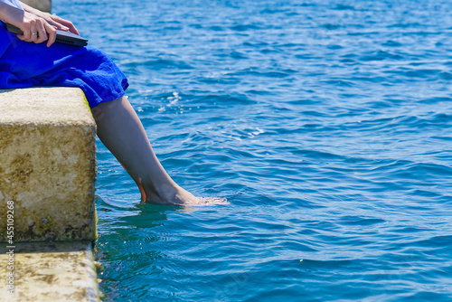 Work from anywhere. Side view of young woman, female freelancer in straw hat working on laptop while sitting on the beach. young woman in sitting on stone at sea and remotely working on laptop