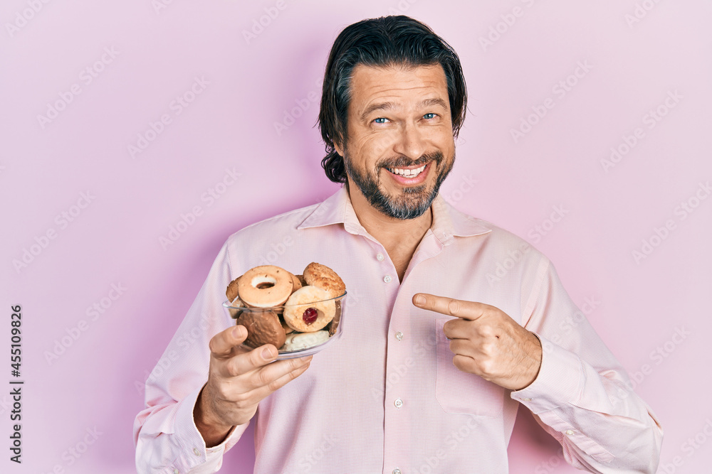 Middle age caucasian man holding sweet pastries smiling happy pointing with hand and finger Middle age caucasian man holding sweet pastries smiling happy pointing with hand and finger