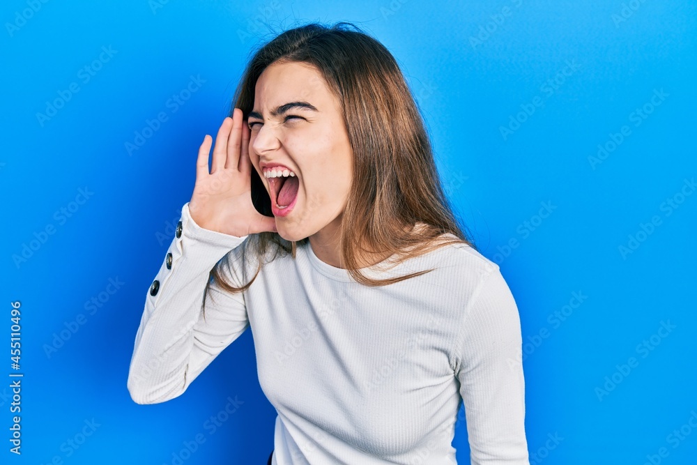 Young caucasian girl wearing casual clothes shouting and screaming loud to side with hand on mouth. communication concept. Young caucasian girl wearing casual clothes shouting and screaming loud to side with hand on mouth. communication concept.