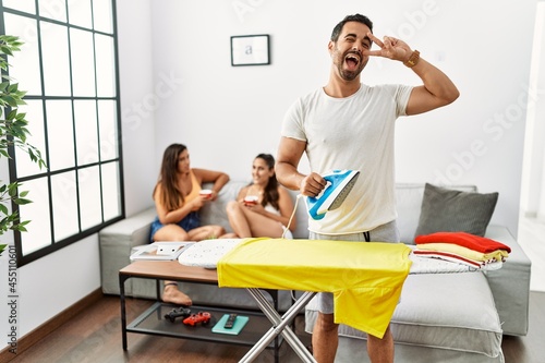 Young hispanic man ironing clothes at home doing peace symbol with fingers over face, smiling cheerful showing victory © Krakenimages.com