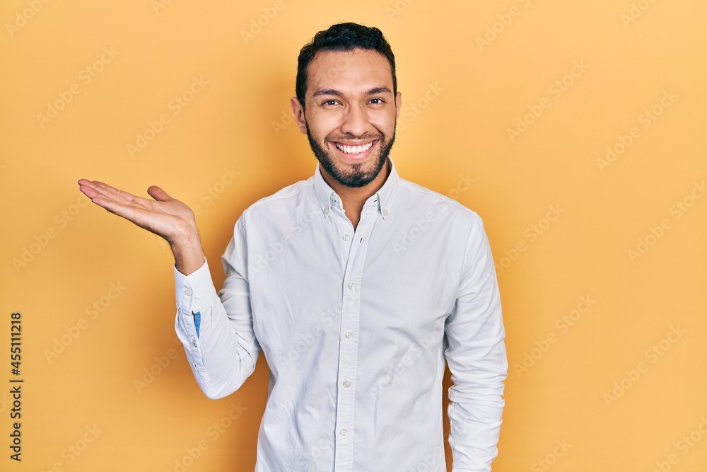 Hispanic man with beard wearing business shirt smiling cheerful presenting and pointing with palm of hand looking at the camera.