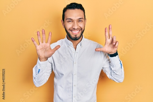 Hispanic man with beard wearing business shirt showing and pointing up with fingers number eight while smiling confident and happy. © Krakenimages.com