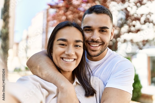 Young latin couple smiling happy and hugging making selfie by the camera at the city.