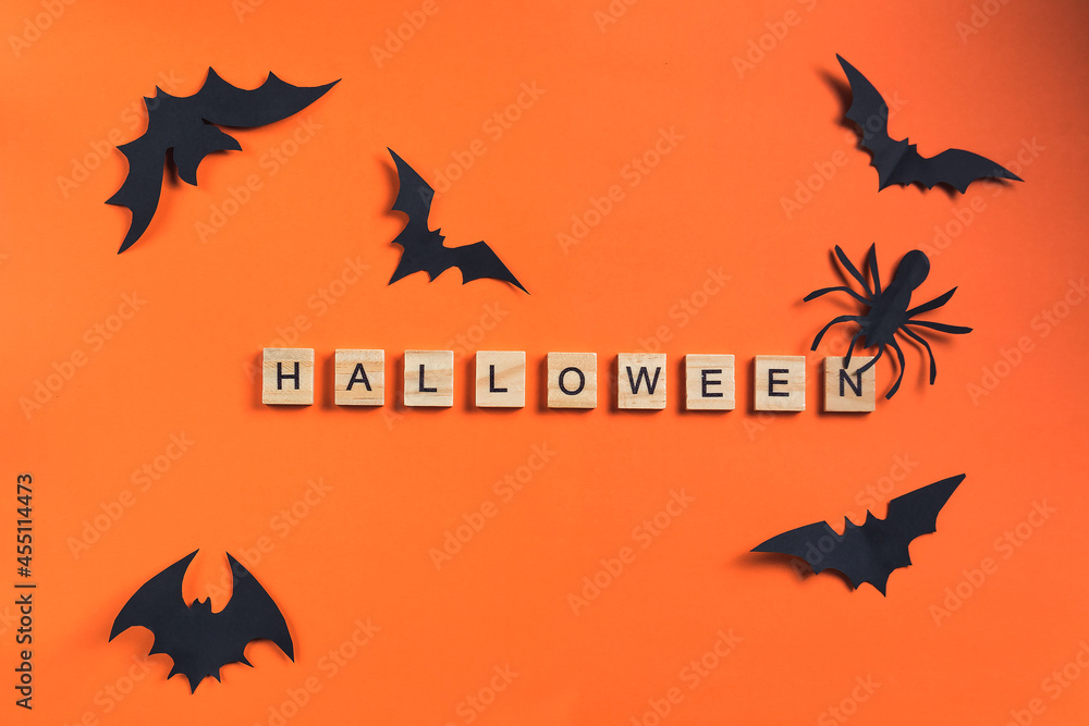 The inscription from wooden cubes and bats cut from black paper on an orange background. Halloween concept and paper decorations. Paper cut style. Flatlay, Copy Space