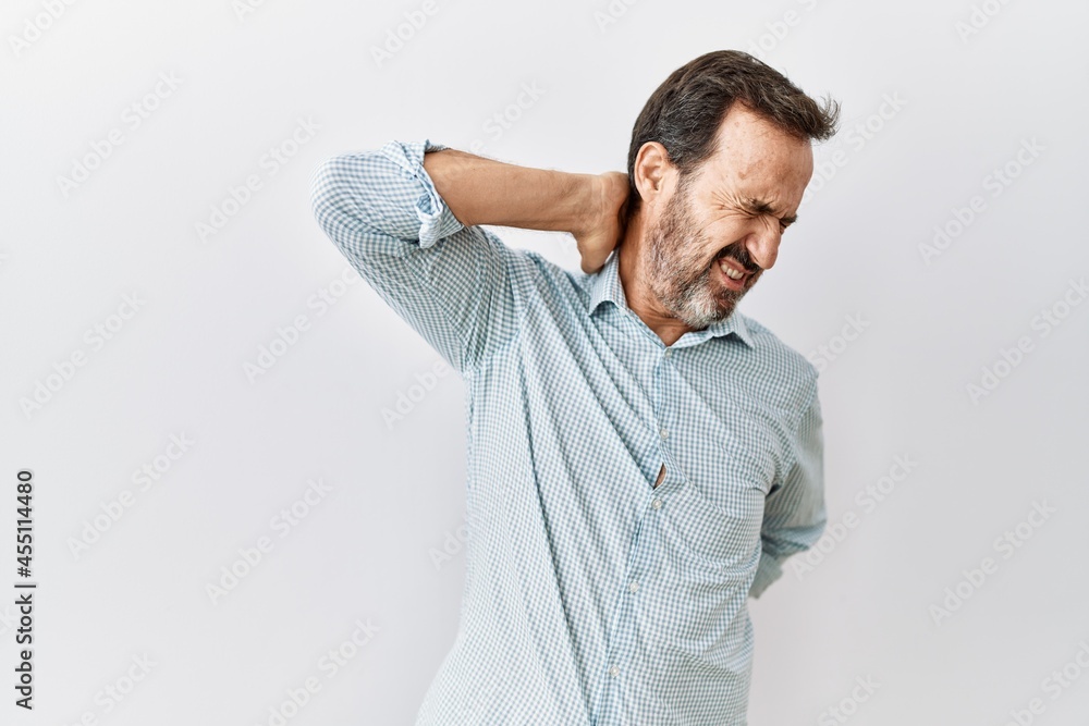 Middle age hispanic man with beard standing over isolated background suffering of neck ache injury, touching neck with hand, muscular pain Middle age hispanic man with beard standing over isolated background suffering of neck ache injury, touching neck with hand, muscular pain