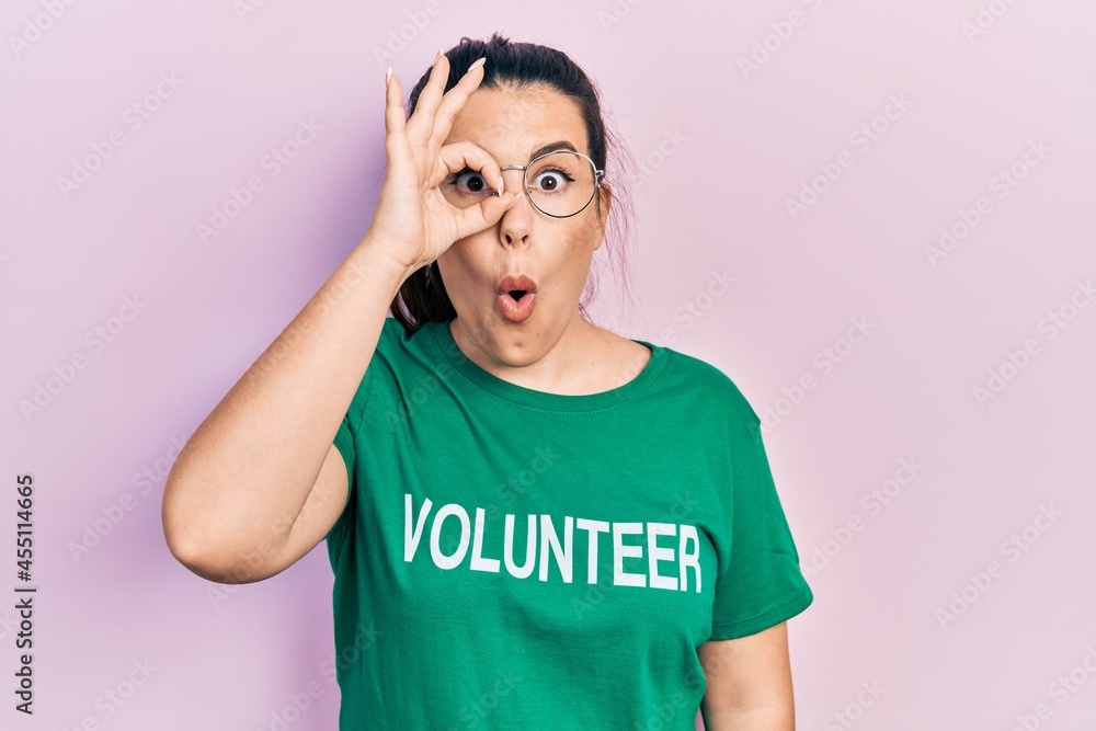 Young hispanic woman wearing volunteer t shirt doing ok gesture shocked with surprised face, eye looking through fingers. unbelieving expression. Young hispanic woman wearing volunteer t shirt doing ok gesture shocked with surprised face, eye looking through fingers. unbelieving expression.