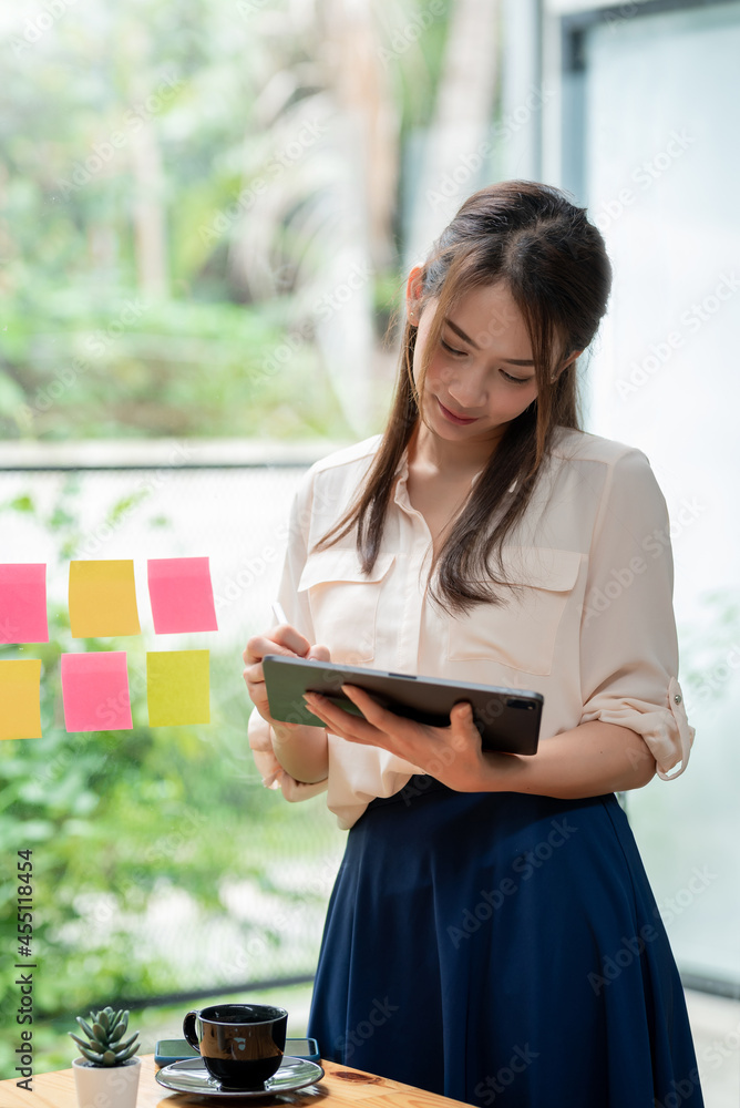 Happy smiling young Asian Businesswoman standing at the mirror holding a pen with a tablet note paper on glass. Happy smiling young Asian Businesswoman standing at the mirror holding a pen with a tablet note paper on glass.