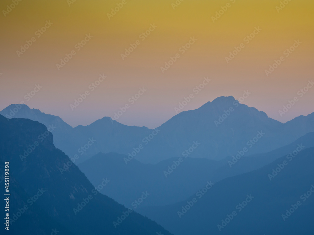 Sunset on the mountain peaks. Silhouette of the outline of the mountains. Warm colors of the sky. Italian Alps. Humidity in the bottom of the valley