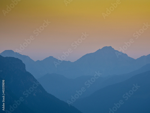 Sunset on the mountain peaks. Silhouette of the outline of the mountains. Warm colors of the sky. Italian Alps. Humidity in the bottom of the valley