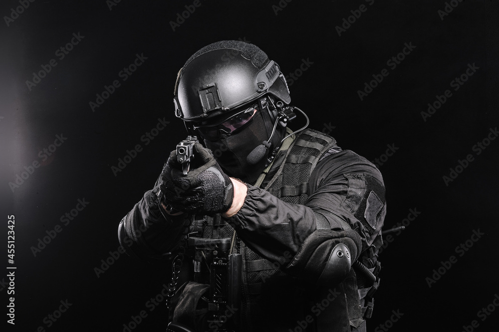A man in glasses, a helmet and a bulletproof vest aims at the camera, photo on a black background.