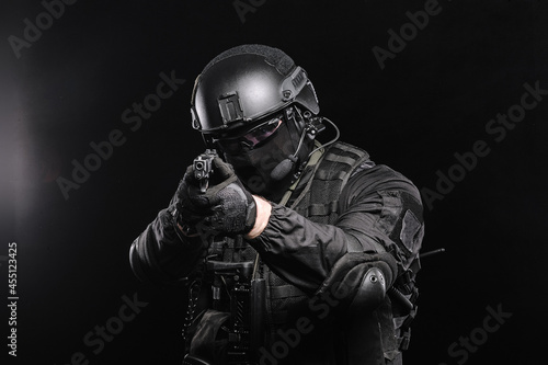 A man in glasses, a helmet and a bulletproof vest aims at the camera, photo on a black background.