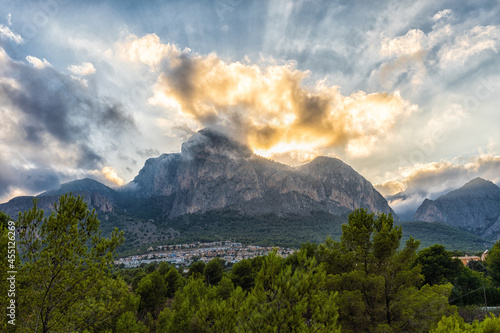 Mountainous landscape. The sun hides behind the mountains, with the cloudy sky.  photo