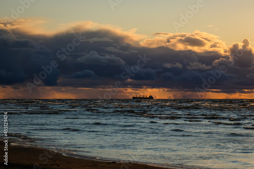 Sun setting at the sea with sailing cargo ship, scenic view. Clouds and storming sea. Defocused.