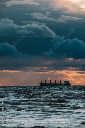 Sun setting at the sea with sailing cargo ship, scenic view. Clouds and storming sea. Defocused.