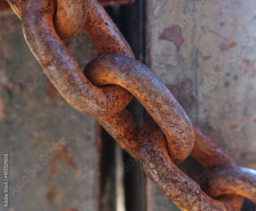 line of rusty heavy links of a thick chain locking a door - closeup of an industrial object © Domingo