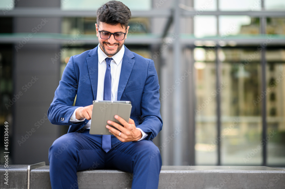 Young manager using his tablet sitting on a bench outdoor in a modern city Young manager using his tablet sitting on a bench outdoor in a modern city
