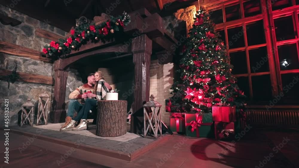 Young people in love near fireplace at Christmas. Happy man and woman sitting together in the country house. Beautiful Christmas tree in the room. Young people in love near fireplace at Christmas. Happy man and woman sitting together in the country house. Beautiful Christmas tree in the room.