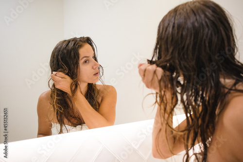 young beautiful millennial brunette white woman at home no makeup wet hair after shower looking at herself at the bathroom mirror while scrunching her wavy hair doing self care routine self love