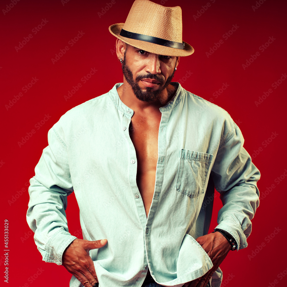 Portrait of a confident and sexy man in a hat and shirt on a red background. A brutal bearded Cuban or Latino poses for the camera. Portrait of a confident and sexy man in a hat and shirt on a red background. A brutal bearded Cuban or Latino poses for the camera.