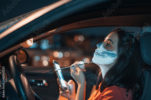 Niña joven maquillandose con un pincel en el coche con el telefono movil para la noche de Halloween junto a la iluminación photo