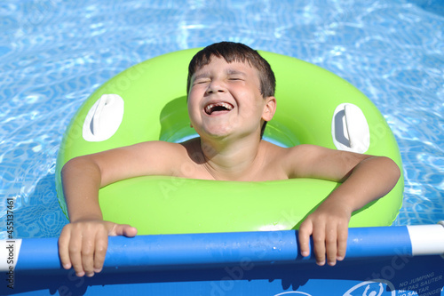 niño desdentado riendo en la piscina con un flotador verde photo